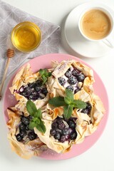 Tasty puff pastries with blueberries, powdered sugar, mint, honey and coffee on white table, flat lay