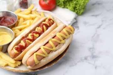 Tasty hot dogs with fries served on white marble table, closeup. Space for text