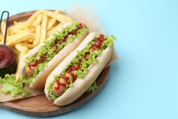 Tasty hot dogs with lettuce, ketchup and potato fries on light blue background, closeup. Space for text