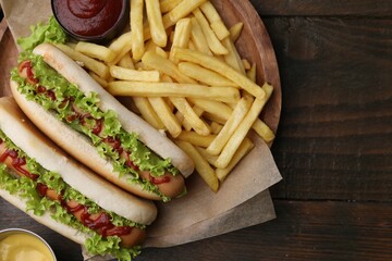 Tasty hot dogs with lettuce, ketchup and potato fries on wooden table, top view