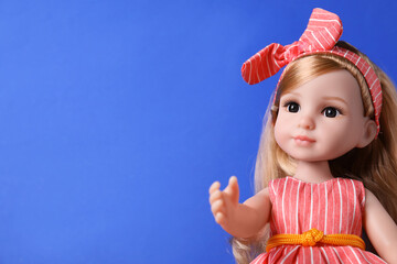 Beautiful doll in dress and headband on blue background, closeup. Space for text