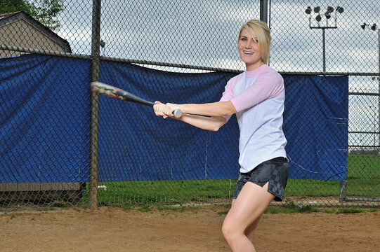 Stunning young blonde female softball player in pink and white baseball jersey shirt - holding bat and swinging - Powered by Adobe