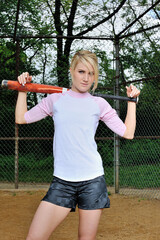 Stunning young blonde female softball player in pink and white baseball jersey shirt - holding bat...