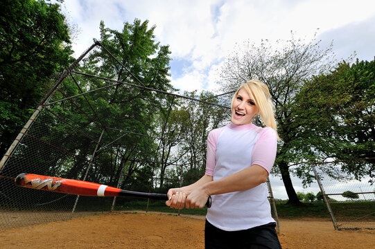 Stunning young blonde female softball player in pink and white baseball jersey shirt - holding bat and swinging - shot with fisheye lens
