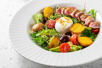 A vibrant salad featuring sliced seared tuna, mixed greens, roasted potatoes, cherry tomatoes, and a soft poached egg, drizzled with a light dressing, served in an elegant white bowl.