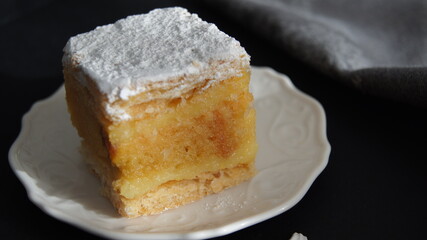 Sponge cake with cream, English soup cake sprinkled generously with powdered sugar, a piece of cake with vanilla cream and impregnation, dessert, on a black background, Italy