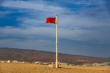 A red flag fluttering in the wind on top of sand dunes, with vast desert landscapes stretching into the distance.