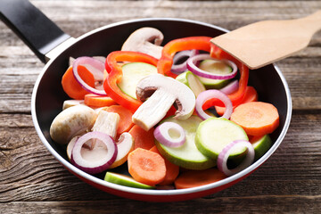 Frying pan with mix of fresh vegetables and mushrooms on wooden table, closeup
