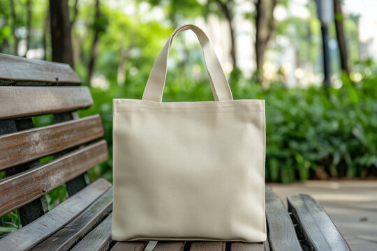 A plain tote bag mockup displayed on a wooden bench in a serene park, surrounded by lush greenery, showcasing its versatility and eco-friendly appeal under natural sunlight.