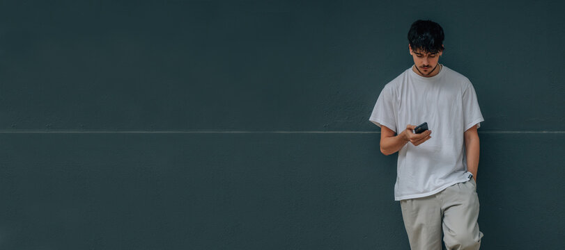 young man on street wall with mobile phone and casual outfit - Powered by Adobe