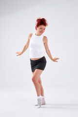 A woman with red hair poses for the camera with a smile on her face, she is wearing a white T-shirt and a black skirt. She has a beautiful figure. Fitness and healthy eating concept.