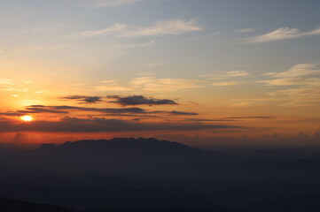 The picture depicts a sunrise on a countryside landscape with foggy mountains and clouds. 