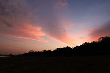 The picture depicts a sunset of a bright pink colour with many clouds.