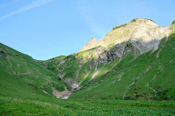 A scenic view of the green mountains of Brienz, Switzerland, showcasing rocky cliffs and lush valleys under a clear blue sky.