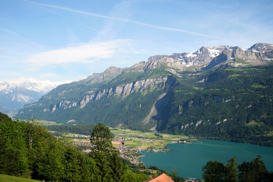 Stunning view of Brienz, Switzerland, featuring majestic mountains, lush green forests, and a serene lake reflecting the clear sky.