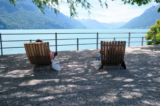 A serene view of two wooden loungers by Lake Brienz in Switzerland, framed by lush mountains and a gentle blue sky, perfect for relaxation.