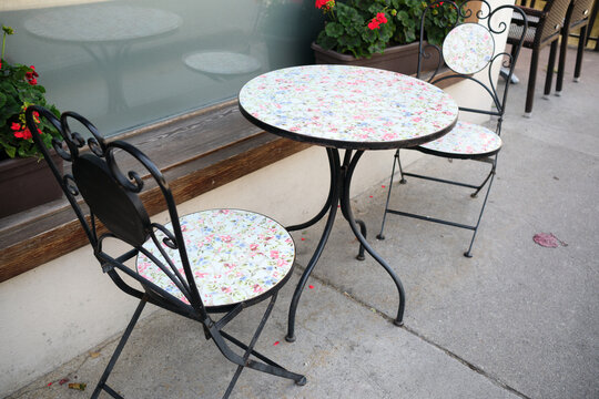 Charming outdoor cafe setup in Brienz, Switzerland, featuring a floral patterned table and chairs. Nearby, vibrant geraniums add a touch of color to the scene.