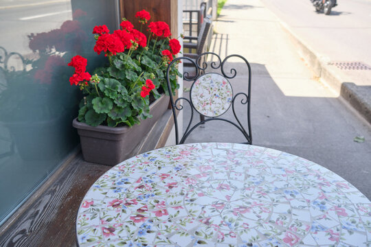Charming outdoor cafe scene in Brienz, Switzerland, featuring a decorative tiled table and a chair beside vibrant red geraniums in a planter.