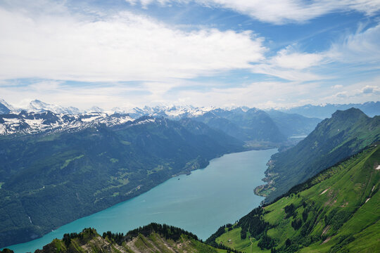 A breathtaking view of Lake Brienz in Switzerland, surrounded by majestic mountains and lush green hills, under a serene sky with wispy clouds.