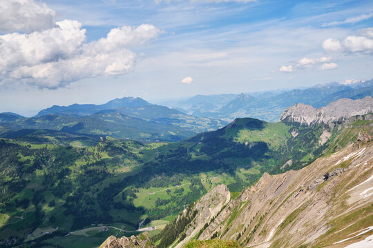 Stunning panoramic view of the Swiss landscape in Brienz, showcasing lush green valleys, rugged mountains, and a clear blue sky with fluffy clouds.