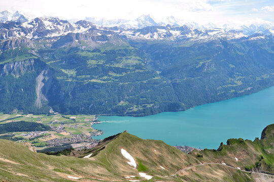 Stunning view of Brienz, Switzerland, featuring lush green hills, turquoise lake, and majestic mountains in the background under a clear blue sky.