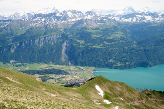 Breathtaking view of the Swiss Alps in Brienz, showcasing lush green valleys, turquoise lake, and snow-capped peaks under a clear sky.
