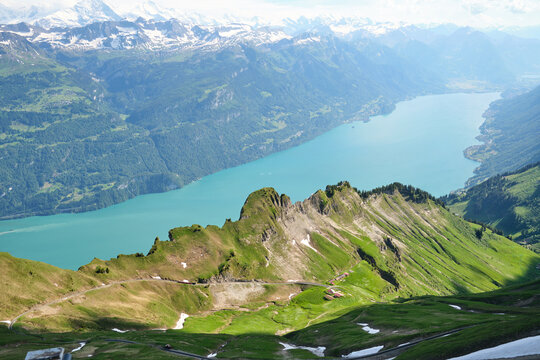Breathtaking view of Lake Brienz, surrounded by emerald hills and majestic mountains in Switzerland. Lush greenery with hints of snow adds to the scenic beauty.