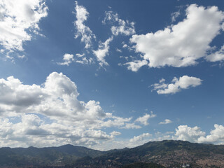 Stunning view of fluffy clouds over a mountain range and city skyline on a bright, sunny day.
