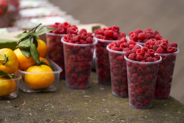 Farmer's market on the street. Plastic cups with ripe raspberries and tangerines in containers.