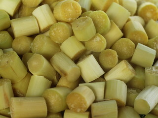 A close-up image of freshly cut sugarcane pieces, revealing the pale yellow-green flesh and fibrous texture.

