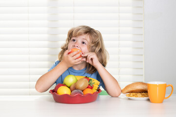 Funny child eating apple. Funny blonde little boy having breakfast. Milk, vegetables and fruits...