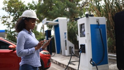 A Black female Electrical engineer is examining the electric vehicle charging pile, EV charger,...