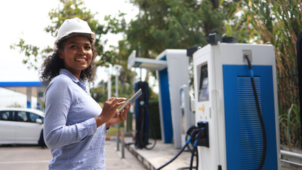 A Black female Electrical engineer is examining the electric vehicle charging pile, EV charger,...