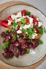 Fried chicken liver and tomato and feta cheese salad garnished with basil