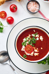Tomato puree soup garnished with parsley, feta cheese and spices with toasted bread slices, tomatoes and herbs on white table