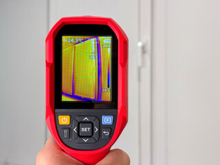 Technician uses thermal imaging camera to identify heat loss and energy inefficiency on building window at winter season