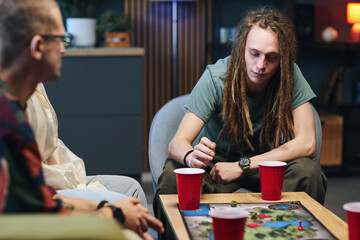 Fototapeta premium Guy making move in board game while playing with his friends at home