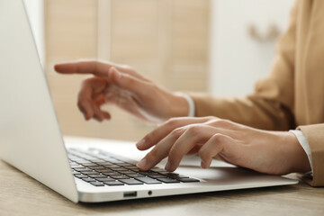 Businesswoman using laptop at wooden table indoors, closeup. Modern technology