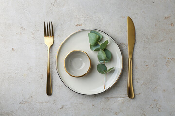 Beautiful plate, sauce bowl and golden cutlery on gray textured table, flat lay