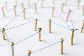 Network connection. Nails linked together by thread on white table, closeup