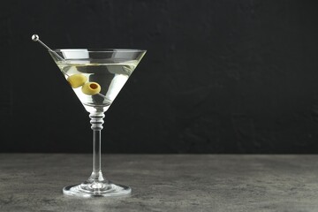 Martini cocktail with olives in glass on grey table against black background, space for text