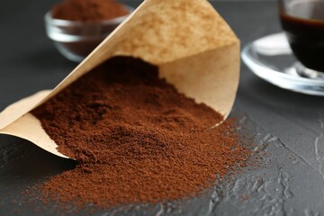 Paper filter, ground coffee and cup of drink on black table, closeup