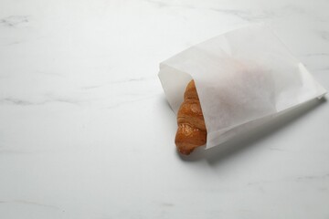 Paper bag with fresh croissant on white marble table, above view. Space for text