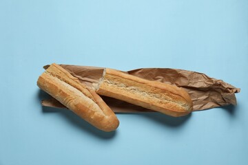 Paper bag and fresh baguette on light blue background, top view