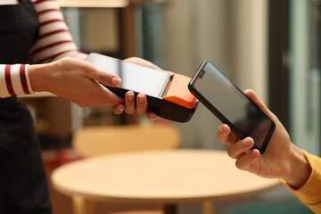 Man paying with smartphone via terminal in cafe, closeup