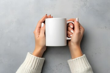 Women's hands hold a mockup of a white empty mug on a gray background