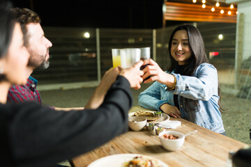 Cheerful friends savoring tacos and drinks, lifting their glasses for a toast at a lively outdoor taco stand