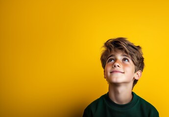 A young boy with tousled hair looks up with curiosity and excitement. He stands in front of a vibrant yellow backdrop, creating a cheerful atmosphere. His expression shows imagination and joy.