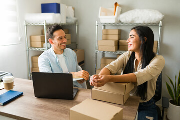 Two cheerful latin entrepreneurs collaborating on sales strategy in their compact warehouse office,...