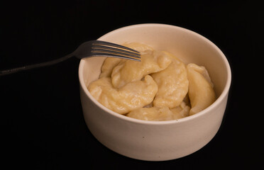The handmade dumplings are cooked in a ceramic bowl on a black kitchen table, with a steel fork next to the plate.